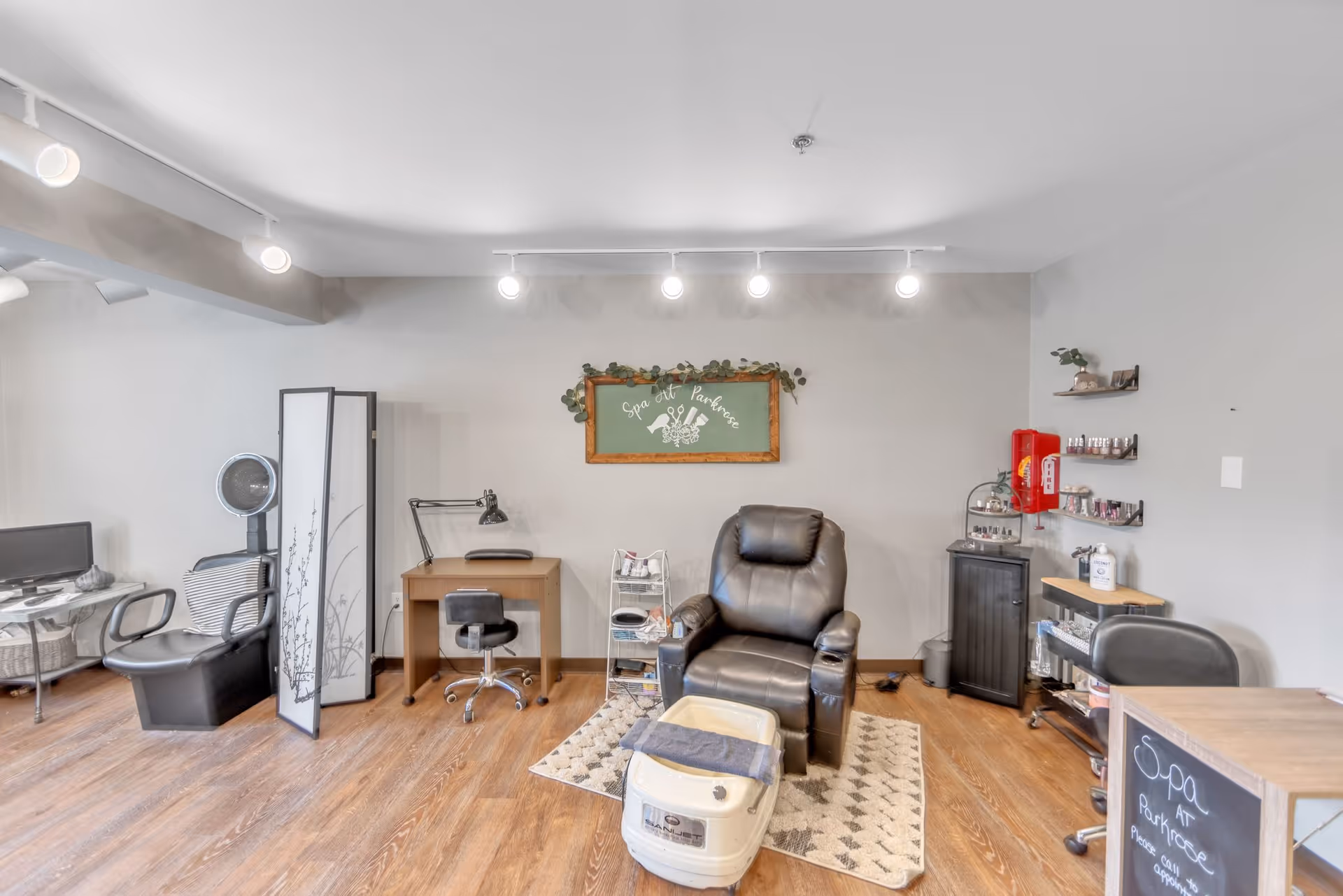 Interior spa room with a leather pedicure chair and foot bath, manicure stations, and shelving.
