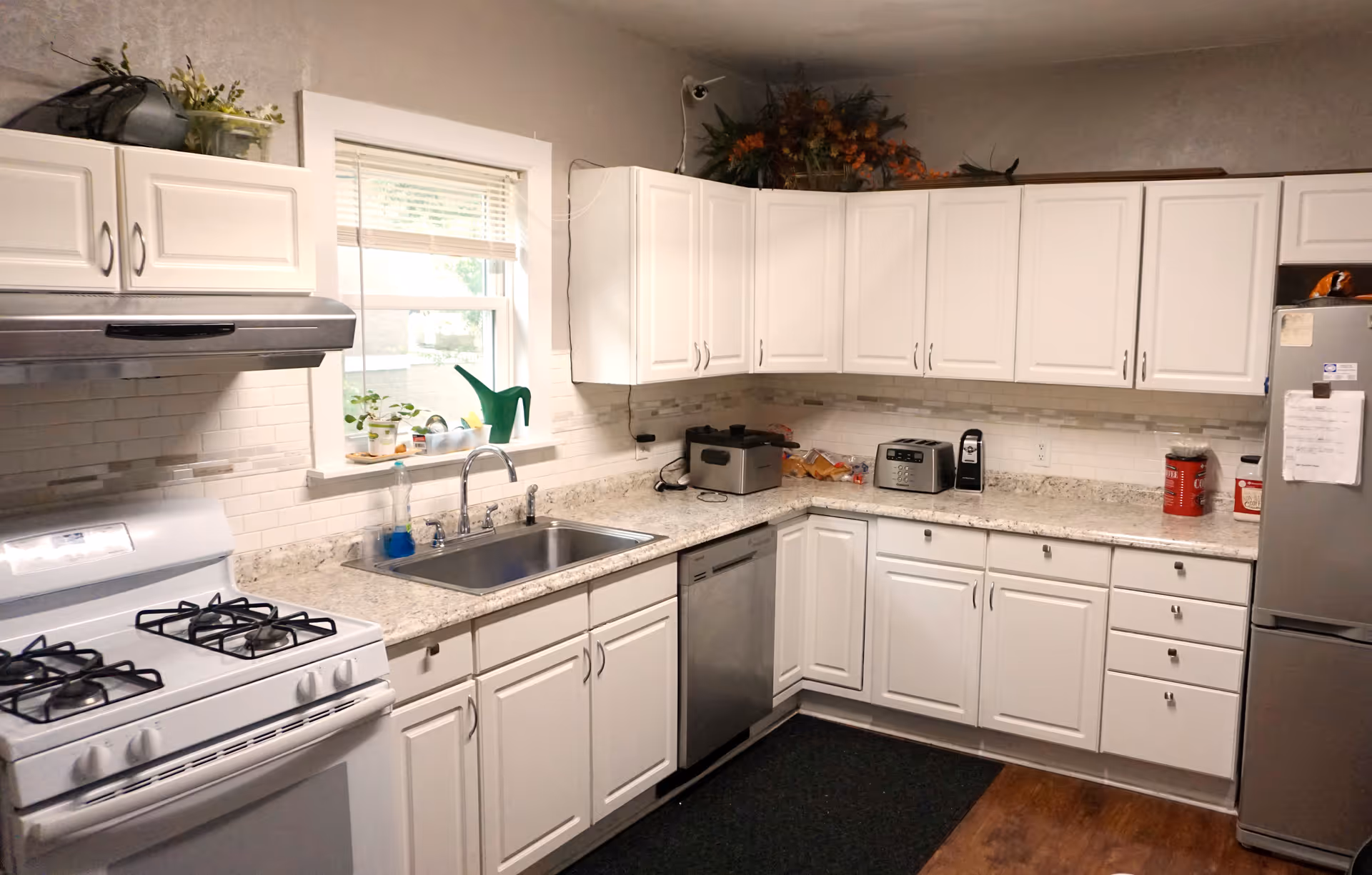 Bright L-shaped kitchen with white cabinets, granite countertops, stainless appliances, and a window over the sink.
