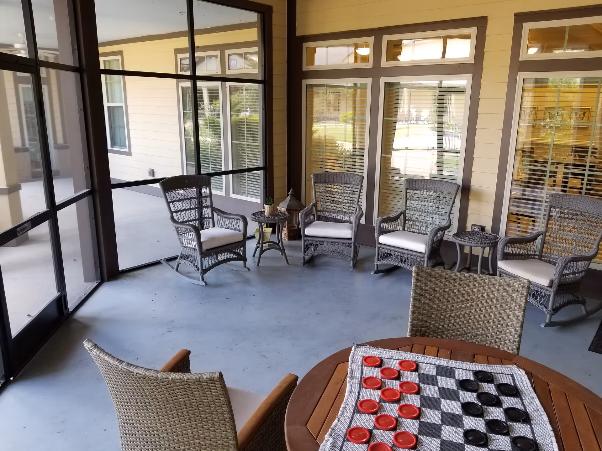 Screened porch seating area with wicker rocking chairs and small tables, and a round table in the foreground with a checkers board and pieces.