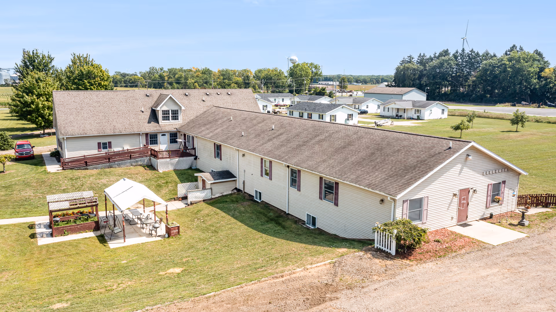 Aerial view of a single-story assisted living building with a grassy courtyard, outdoor pergola seating area, and nearby small homes.