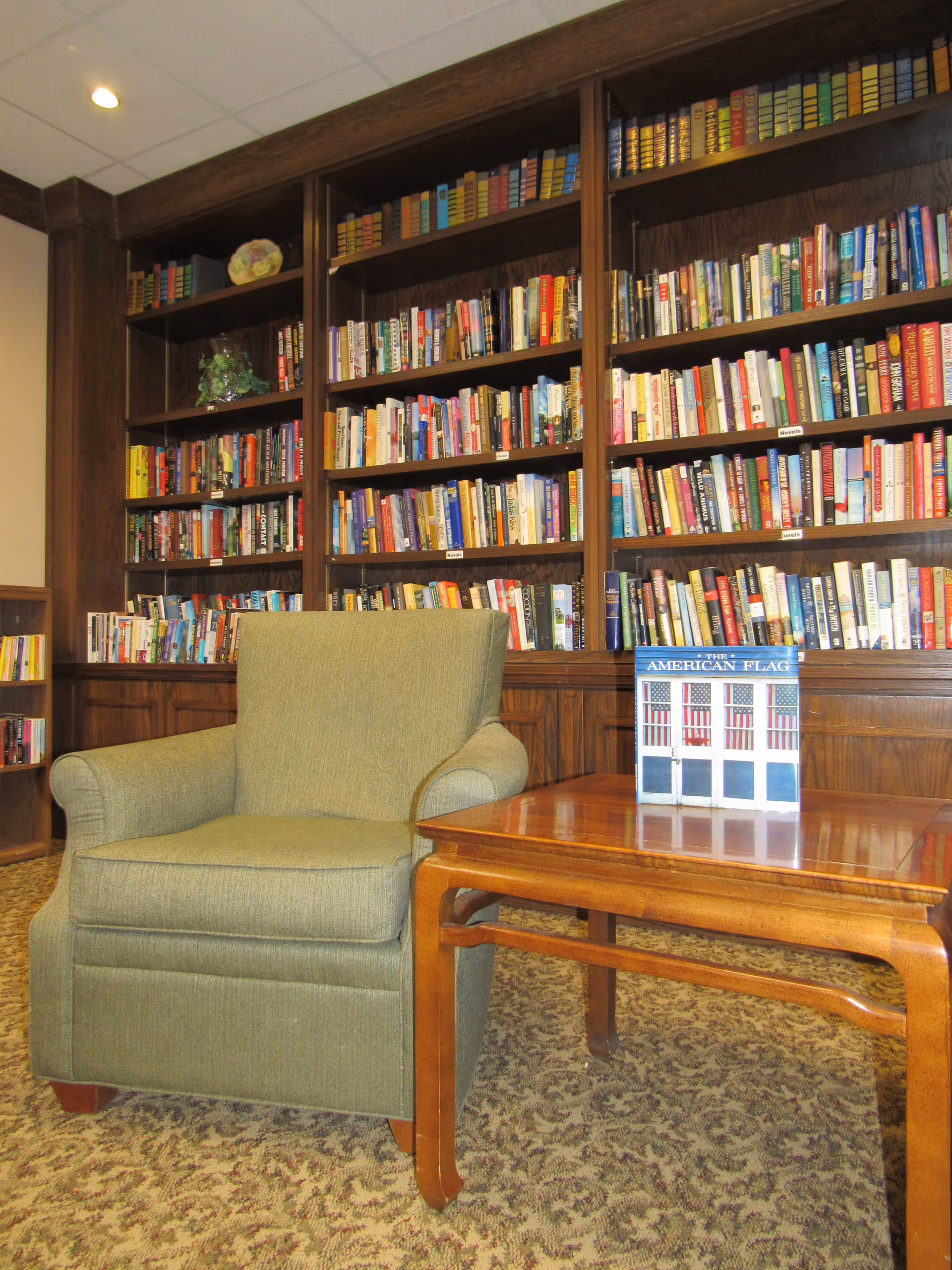 Green armchair and wooden side table in front of floor-to-ceiling bookshelves filled with books in a reading room.