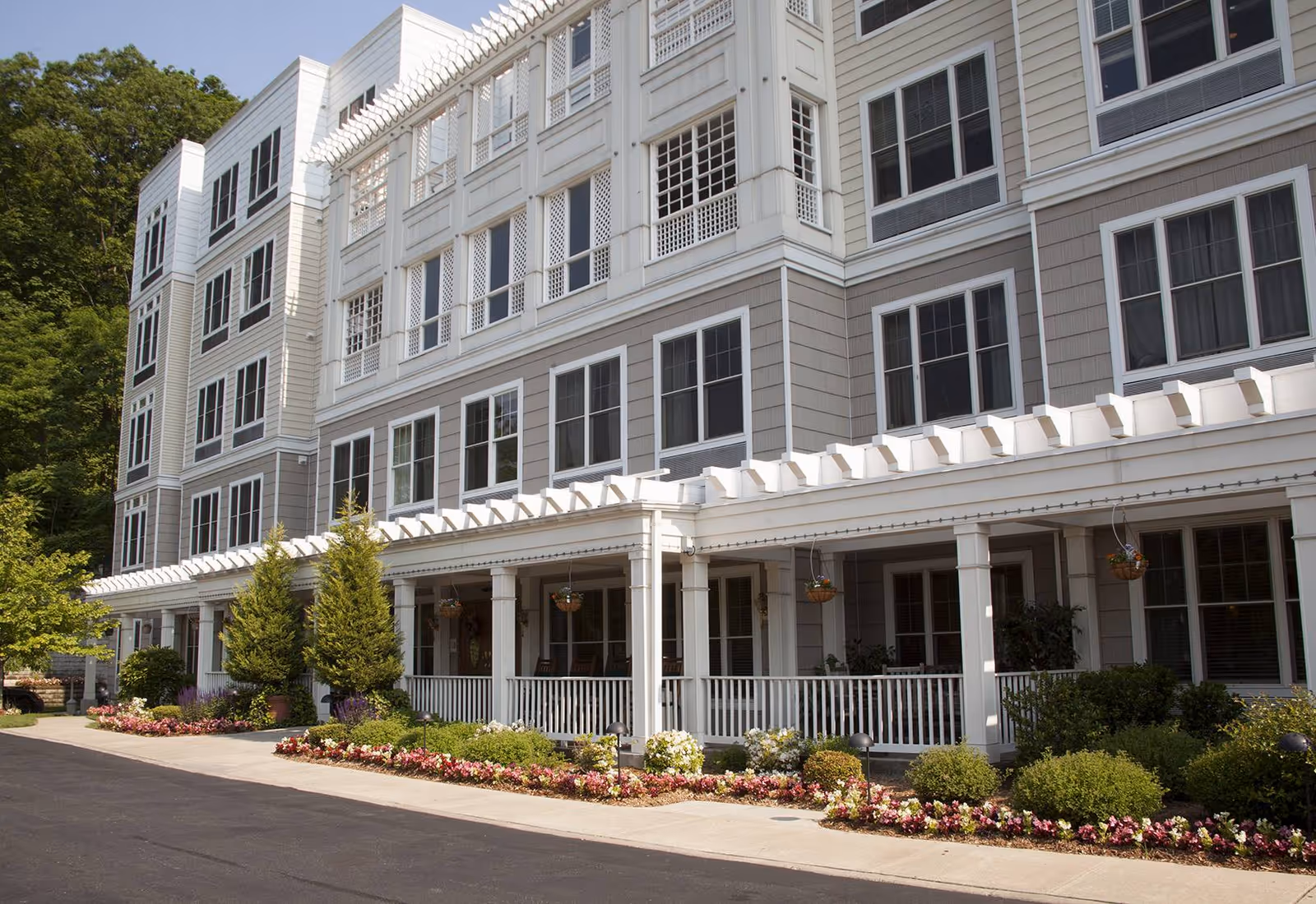 Front exterior of a multi-story senior living building with a covered porch, columns, many windows, and landscaped flower beds.