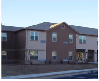Exterior view of a two-story senior living facility building with multiple windows and a main entrance, under a clear sky.