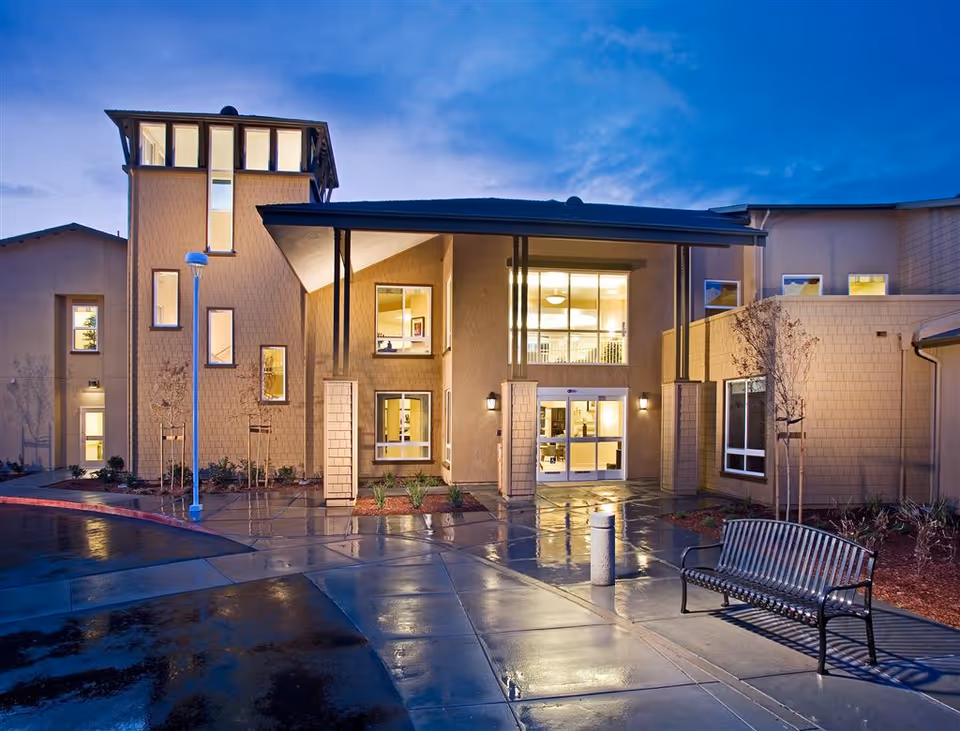 Front entrance of The Parkview building at dusk with illuminated windows, wet pavement, and a bench.