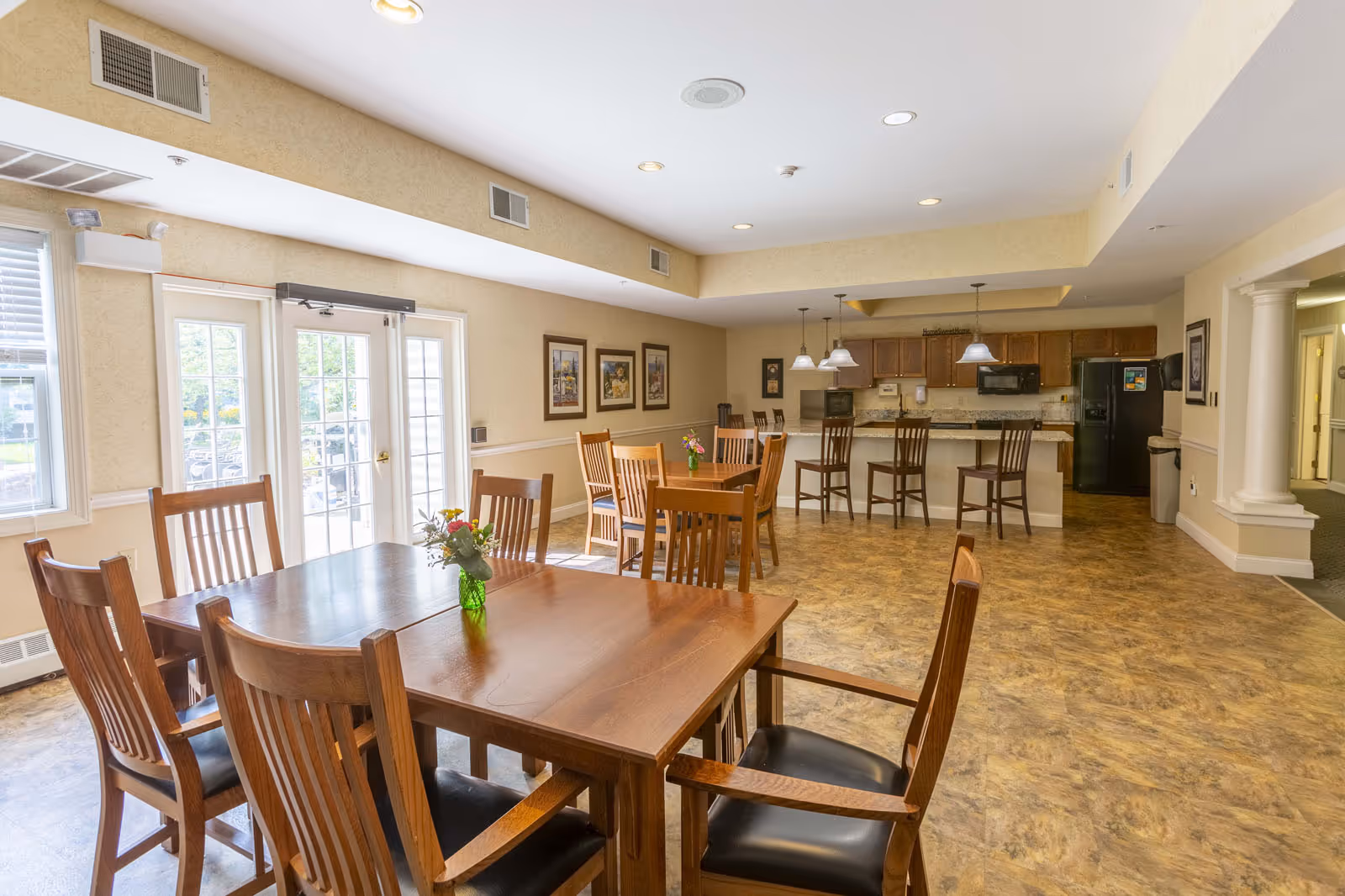 Communal dining area with wooden tables and chairs and a kitchen counter with barstools in the background.