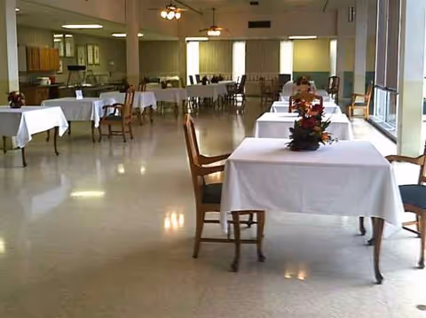 A spacious dining room with white tablecloths, floral centerpieces, and seating.