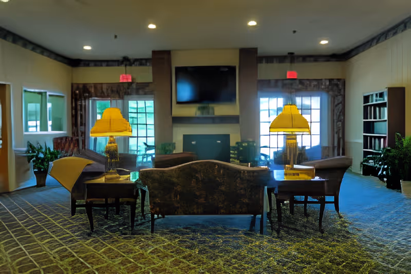 Lobby seating area with sofas, side tables and lamps facing a wall-mounted TV above a fireplace.