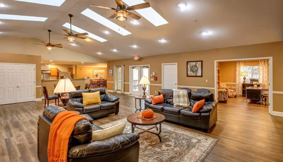 Spacious senior living lounge with leather sofas, coffee tables, and warm lighting.