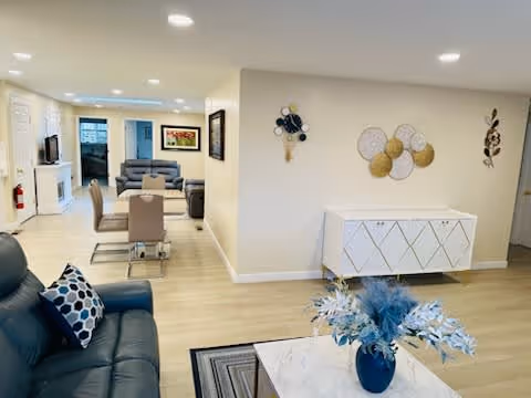 Bright open communal living area with sofas, a dining table, a decorative sideboard, and a coffee table with flowers.