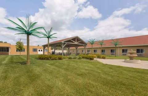 Exterior view of Belle Fountain Nursing & Rehab showing a covered entrance and palm trees.