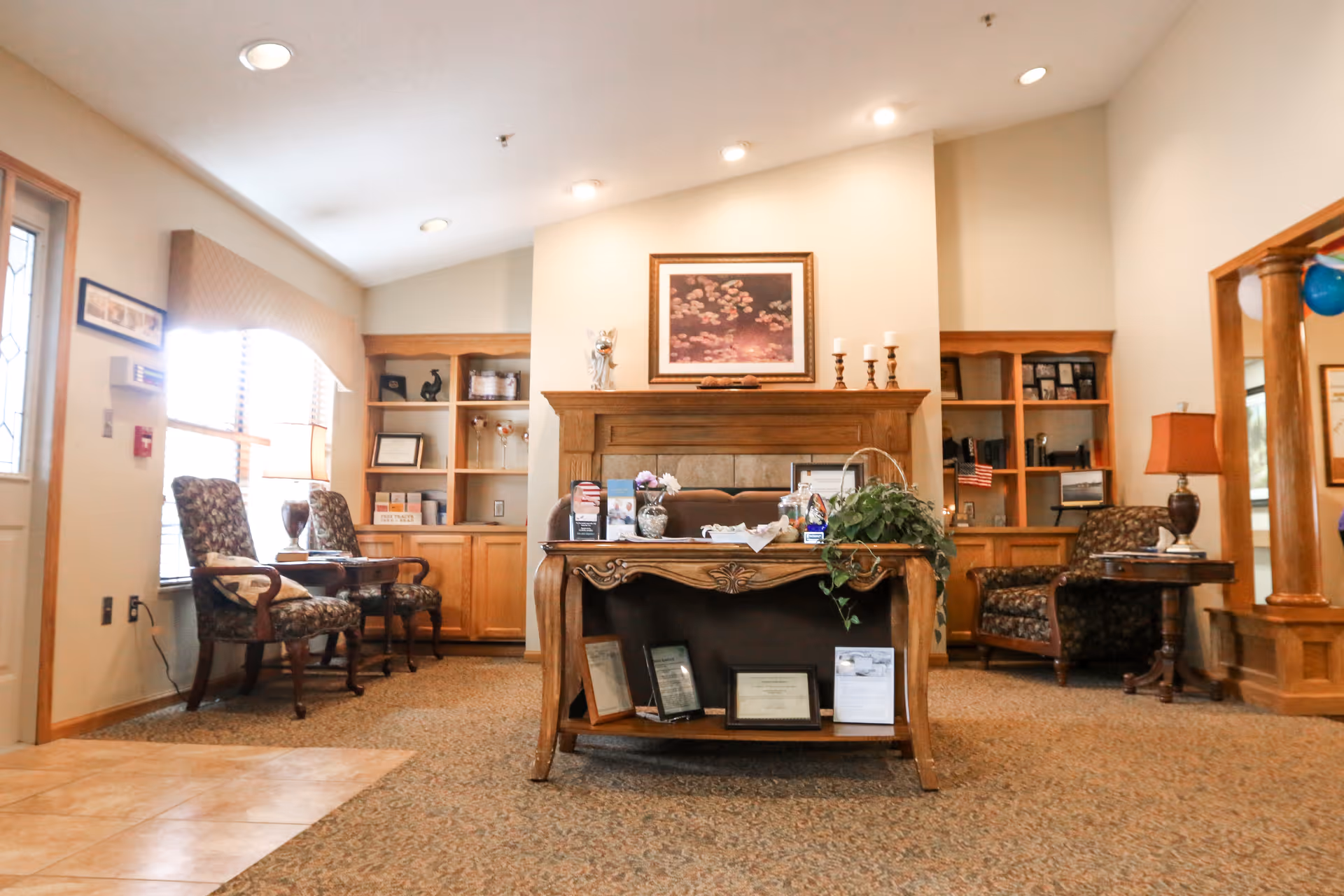 A warm interior reception/lounge area with a wooden front desk, built-in shelving, upholstered chairs and decorative accents.