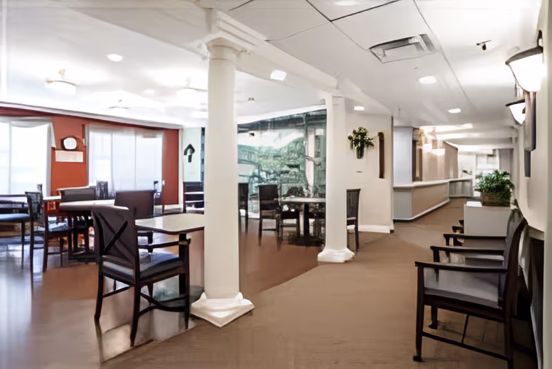 Open dining and lounge area with tables and chairs, white columns, and a hallway with bench seating.