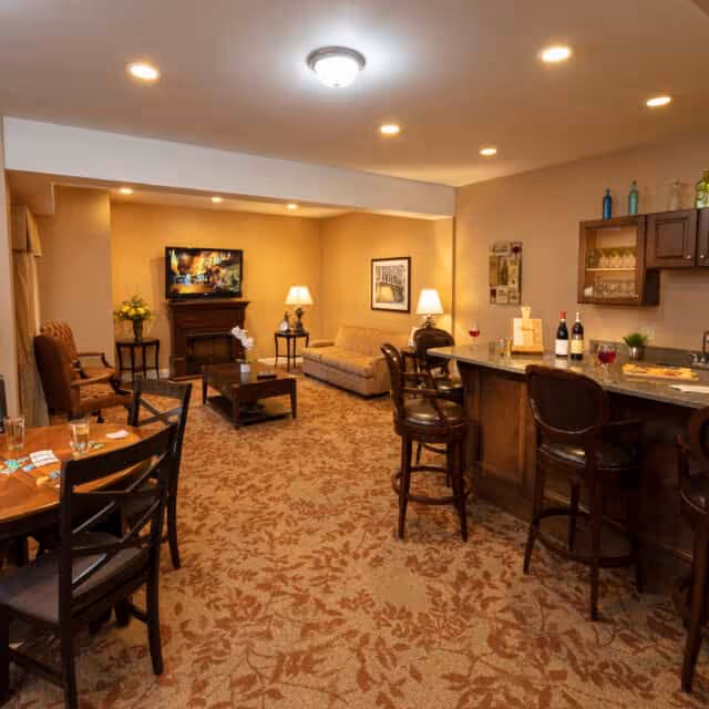 Cozy communal lounge with sofas, chairs, a TV above a fireplace, a dining table and a bar area.