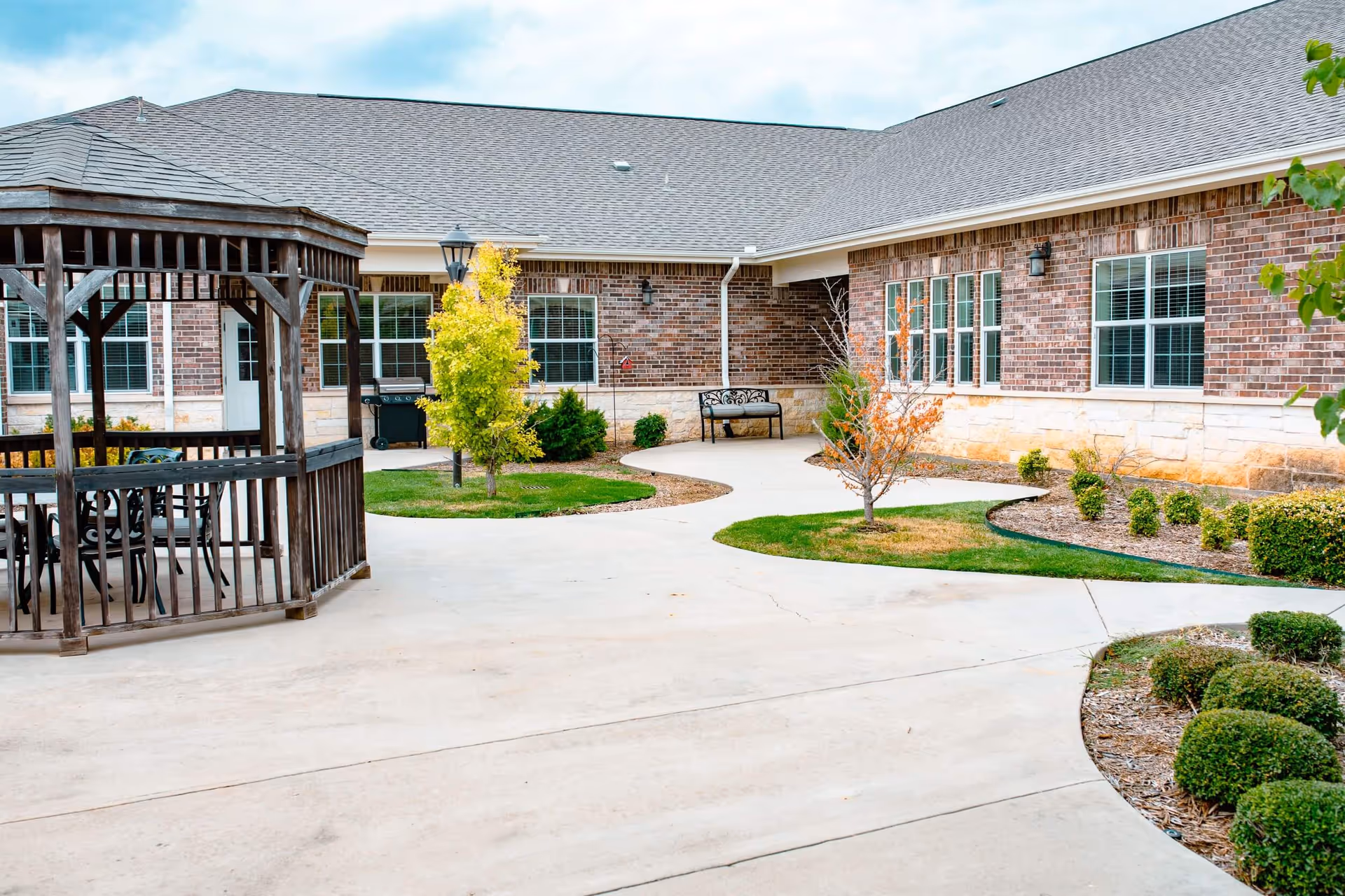 A landscaped exterior courtyard with a wooden gazebo, paved walkways, benches, and a brick building facade.