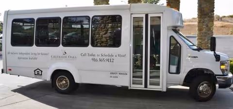White shuttle bus labeled Creekside Oaks Retirement Community parked outside with open door