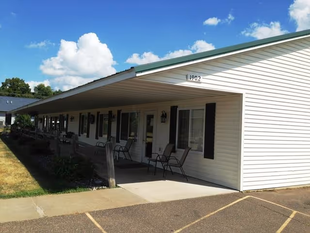 Single-story assisted living building with a long covered front porch, outdoor chairs, and the address number 1902 visible.