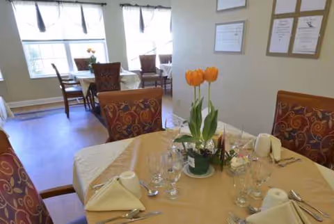 Homey dining room with round tables, beige tablecloths, tulip centerpieces, and place settings.