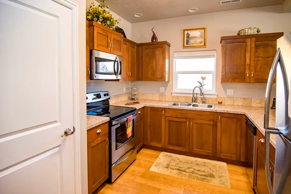 Bright kitchen with wooden cabinets, stainless steel appliances, a double sink beneath a window, and a stove.