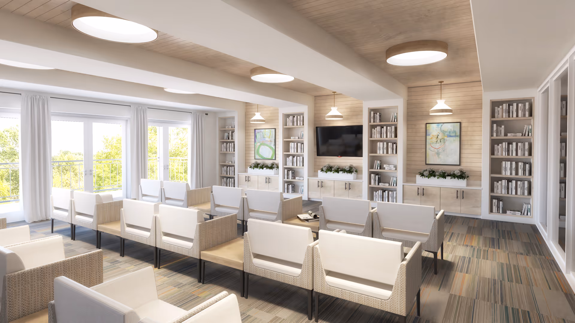 Bright communal lounge with rows of armchairs facing a wall-mounted TV, bookshelves, and large windows.