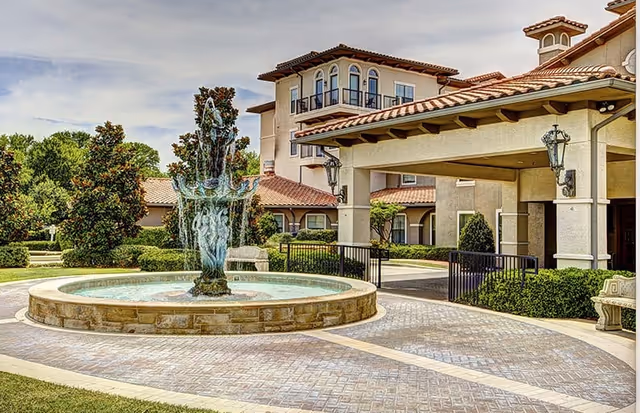 Mediterranean-style building entrance with a circular fountain, covered porte-cochère, and landscaped grounds.