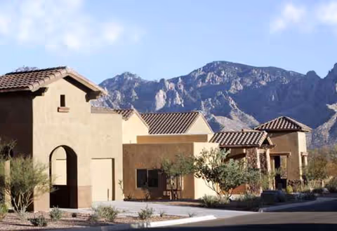 Southwestern-style senior living campus with stucco buildings, tiled roofs, desert landscaping, and mountain backdrop.