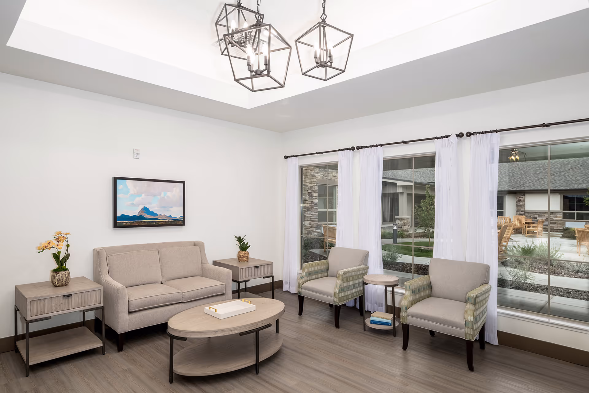 Bright communal living room with a sofa, three armchairs, coffee tables and large windows overlooking a courtyard.