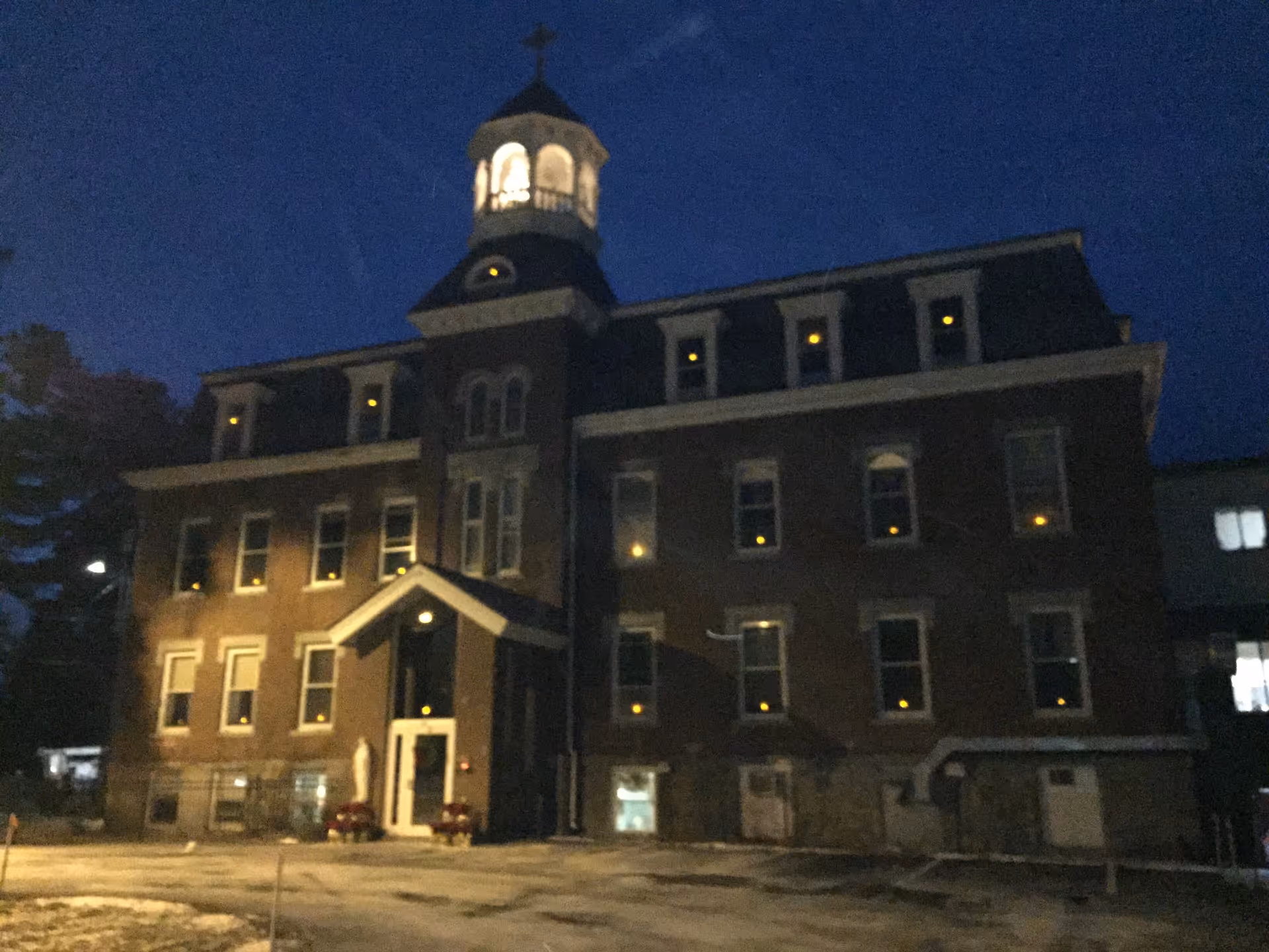 Front exterior of a multi-story brick building with an illuminated cupola and many lit windows at night.
