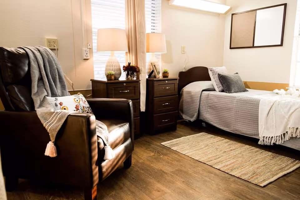 A cozy nursing facility bedroom with a single bed, leather armchair, bedside tables and lamps.