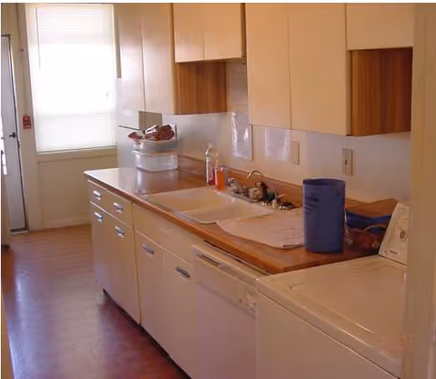 Senior living facility kitchen with white cabinets, sink, and appliances along counters.