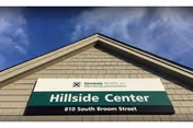 Exterior view of the Hillside Center building showing a sign with the Genesis HealthCare logo and the address 810 South Broom Street under a blue sky with some clouds.