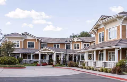 Exterior view of Sunrise of Carmichael building with porches, shrubs, and a paved driveway.