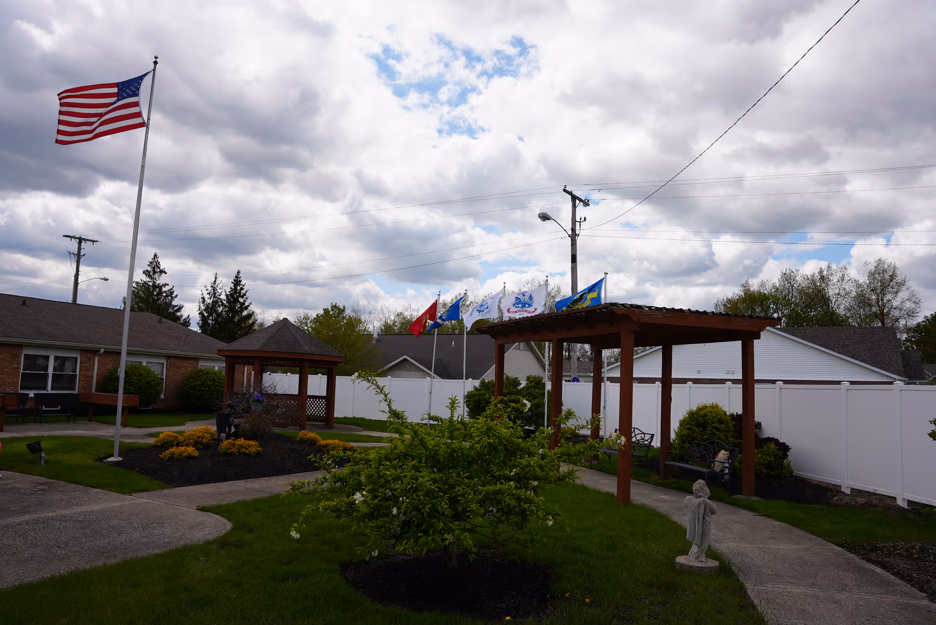 Outdoor courtyard with an American flag, pergola, gazebo, walkways, and landscaped beds.