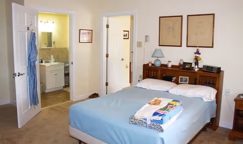 Bedroom with a made bed, headboard and nightstand, and an open door leading to a bathroom.