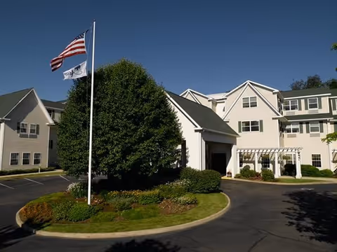 Exterior view of a senior living facility with flagpole, manicured landscaping, and front entrance