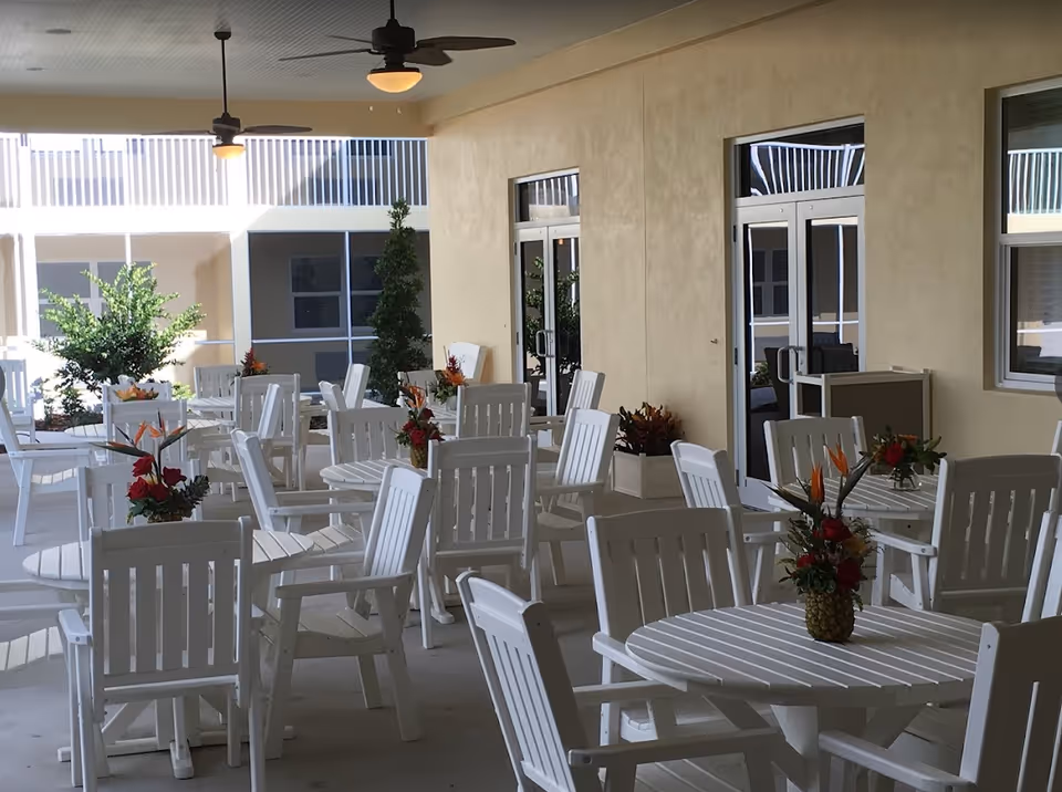 Covered outdoor seating area with multiple white tables and chairs decorated with floral centerpieces.