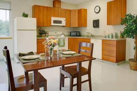 A kitchen and dining area with wooden cabinets, appliances, and a table set for a meal.