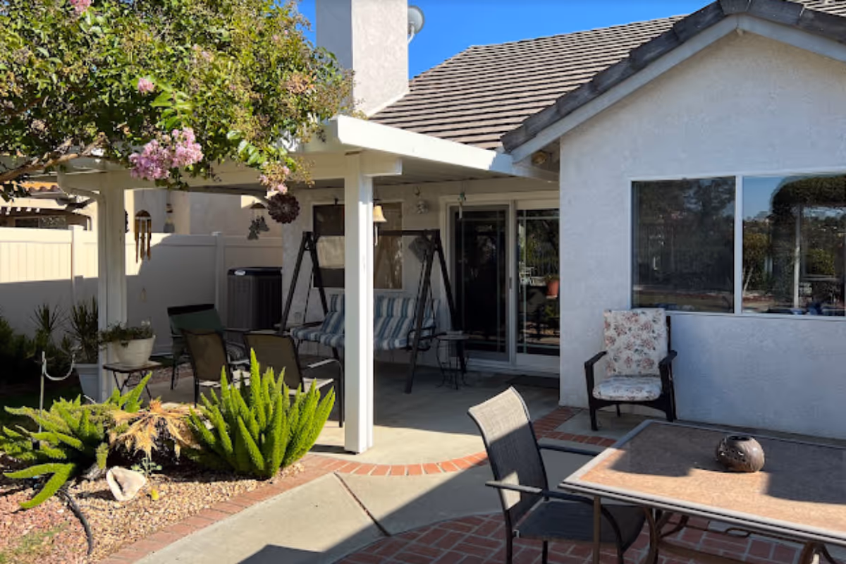 Backyard patio with a covered seating area, outdoor chairs and table, potted plants, and the house exterior.
