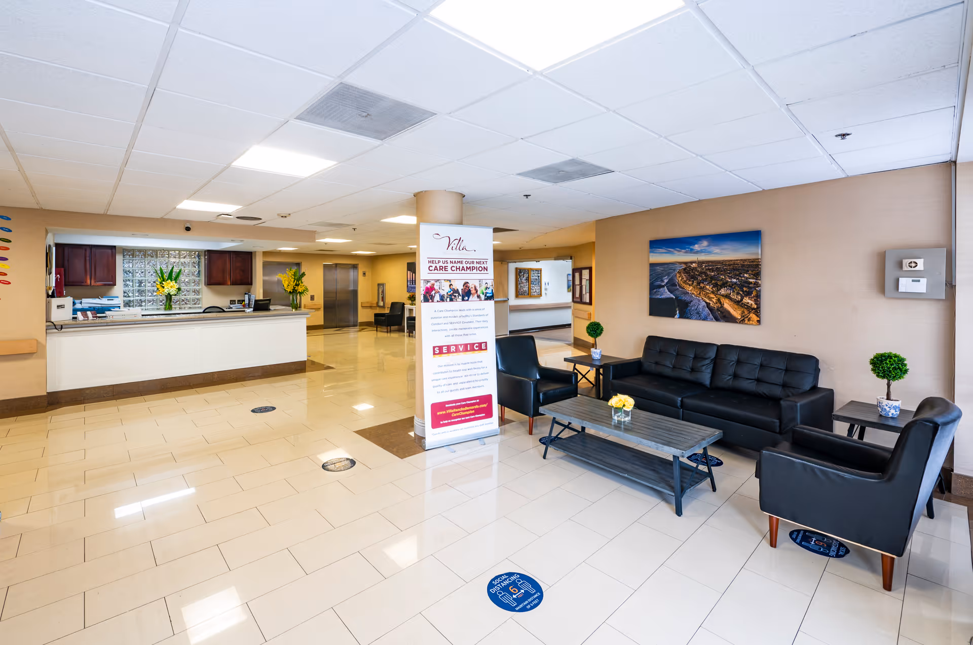 Bright reception lobby with black sofas and chairs, a front desk, and a promotional stand in the center.