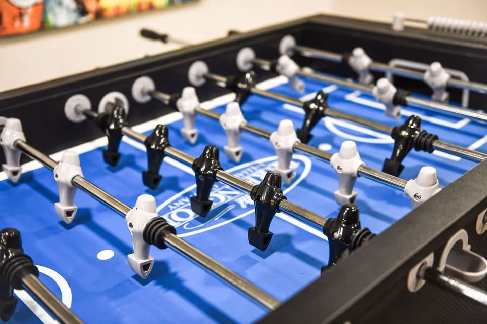 Close-up view of a foosball table with black and white player figures on metal rods, set on a blue playing surface.