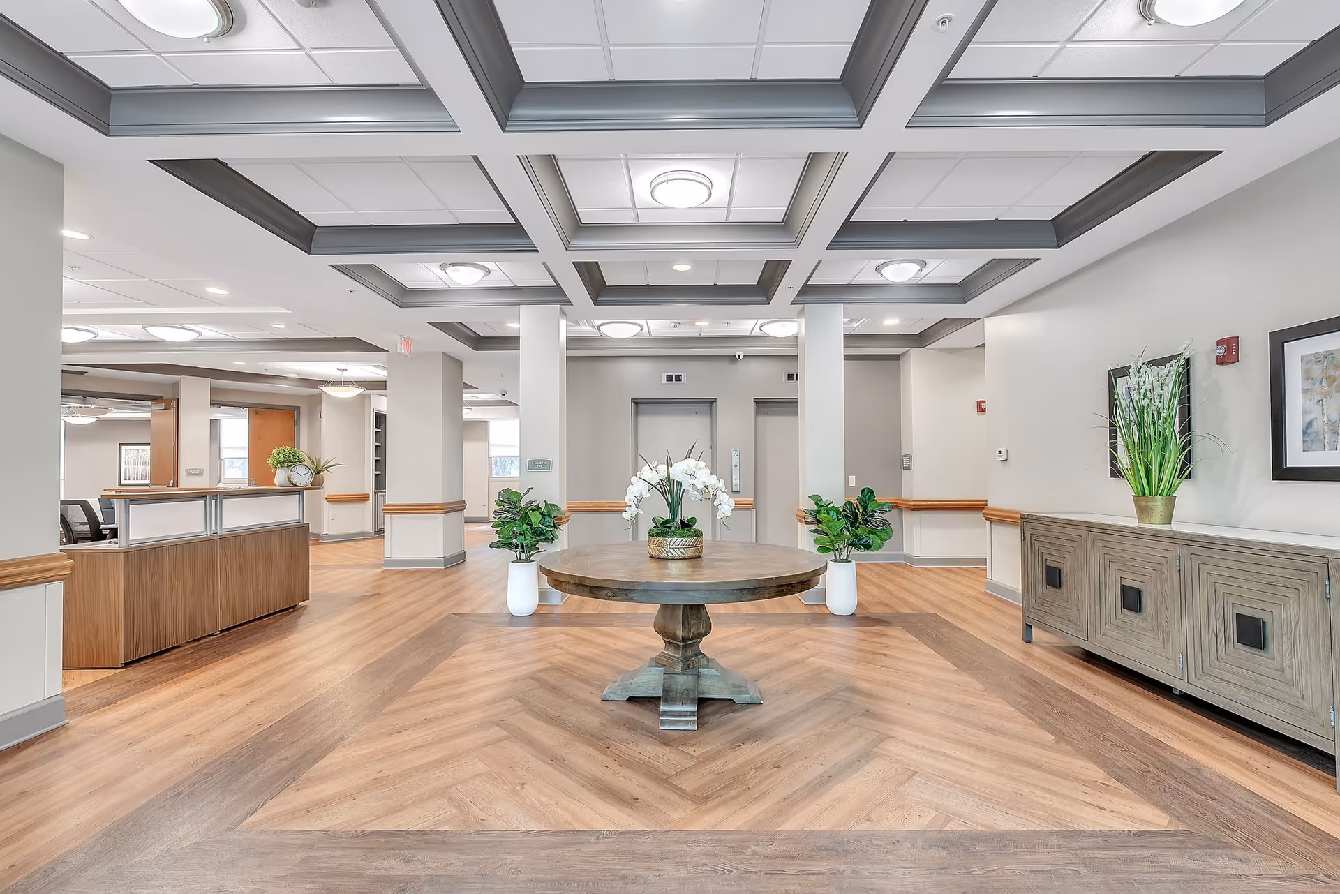 Bright, modern lobby with a central round table decorated with plants and elevators in the background.