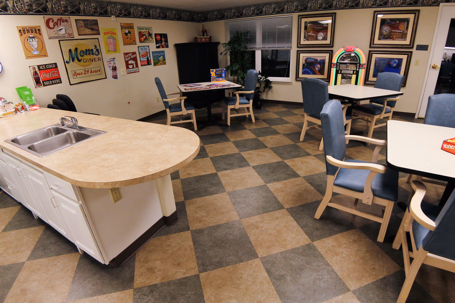 Communal activity/dining room with a kitchenette island, several tables and chairs, a jukebox and retro wall signs.