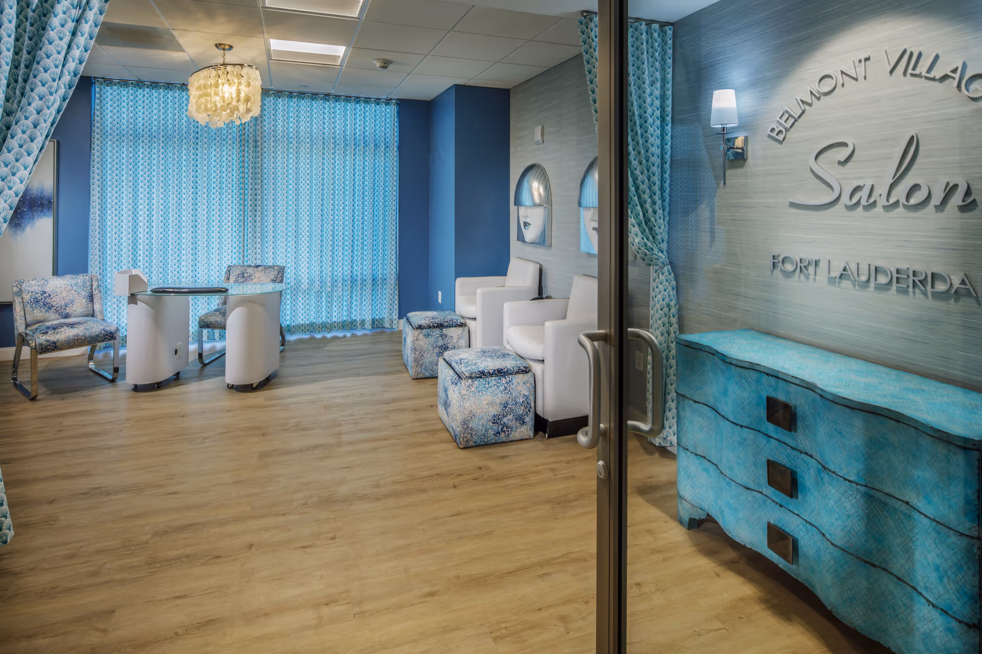 Turquoise-themed salon interior with chairs, pedicure stations, a manicure table and a dresser labeled 'Belmont Village Salon Fort Lauderdale'.