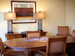 Dining room with a wooden table and chairs, a partially completed puzzle on the table, and a sideboard with lamps and framed artwork.