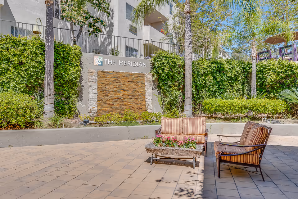 Outdoor courtyard with patio chairs and a planter in front of a stone wall sign that reads "The Meridian".