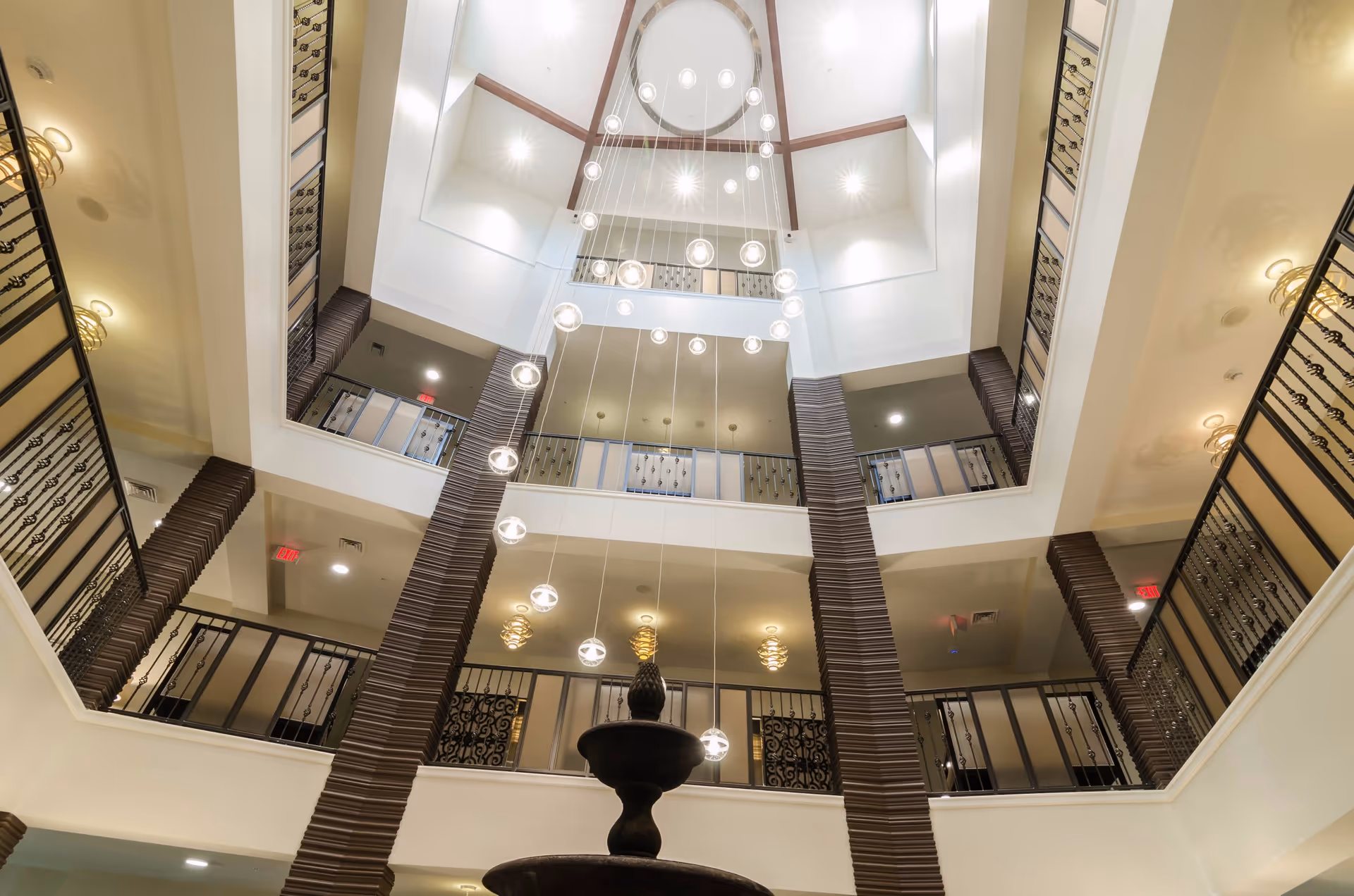Looking up at a multi-story atrium with hanging globe lights, balconies, and decorative railings.