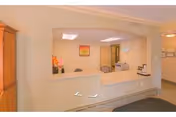 Reception area inside a nursing center with a counter, a chair behind the counter, a framed picture on the wall, and a small flower arrangement on the counter.