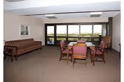 Community lounge with a table and chairs, a sofa, and large windows overlooking an outdoor area.