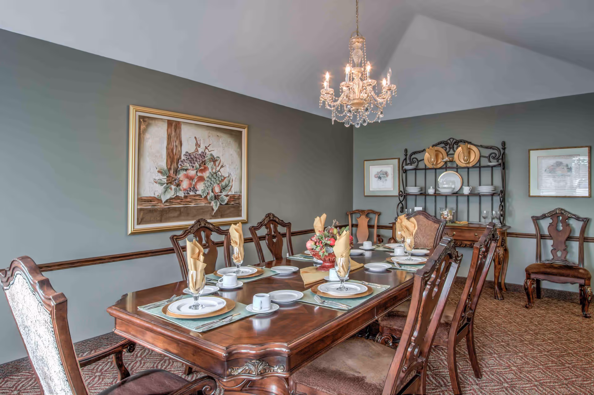 Formal dining room with a long polished wooden table set for a meal, a chandelier overhead, and a hutch against the wall.