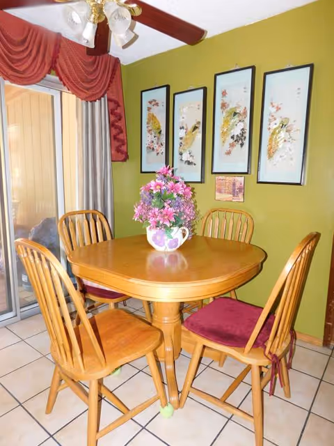 Round wooden dining table with four chairs and floral centerpiece in a green dining area.