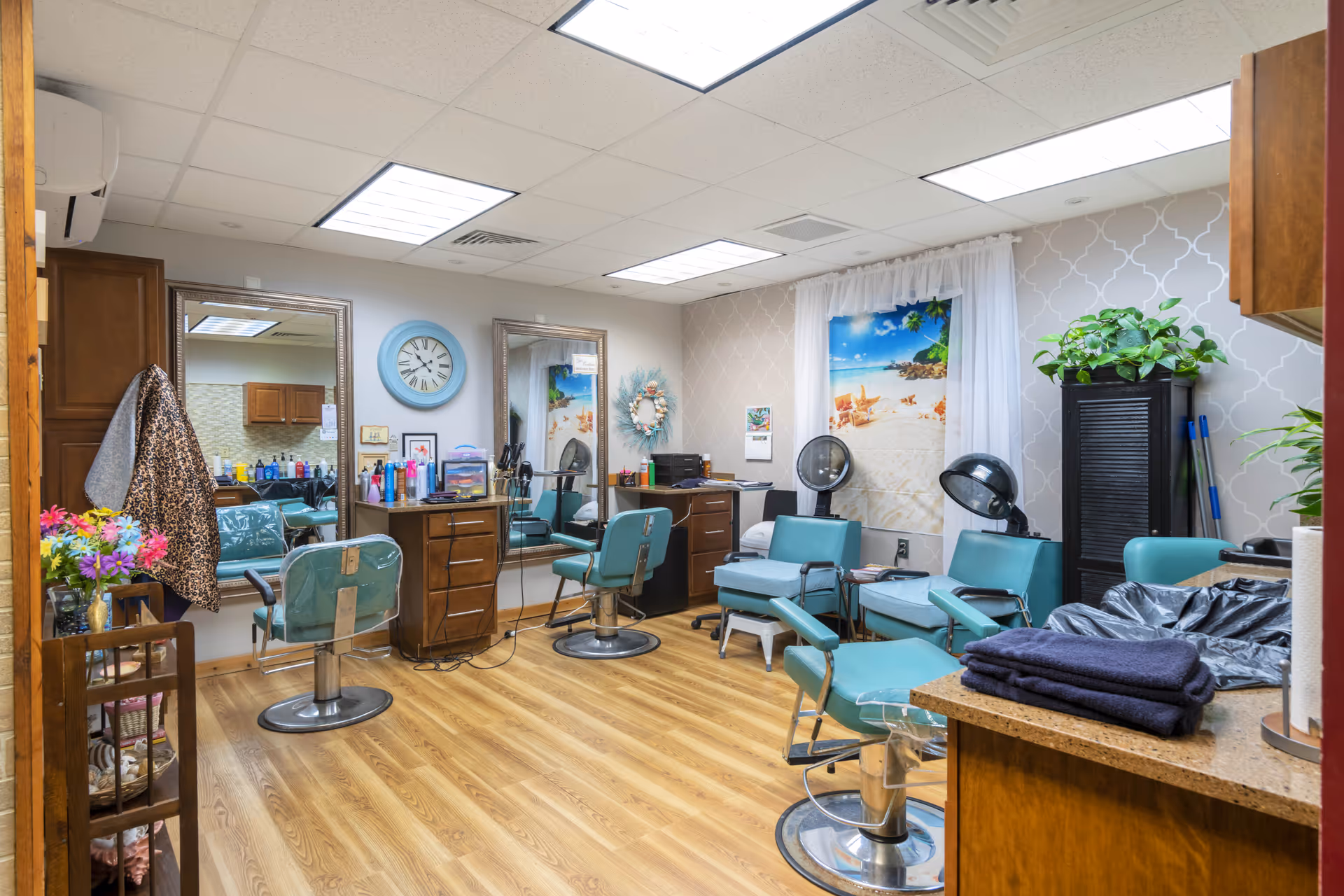 A bright salon inside a senior living facility with teal styling chairs, mirrors, hair stations and hair dryers.
